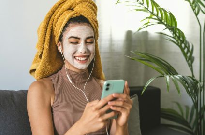Young woman using mobile smartphone while having skin care spa day at home